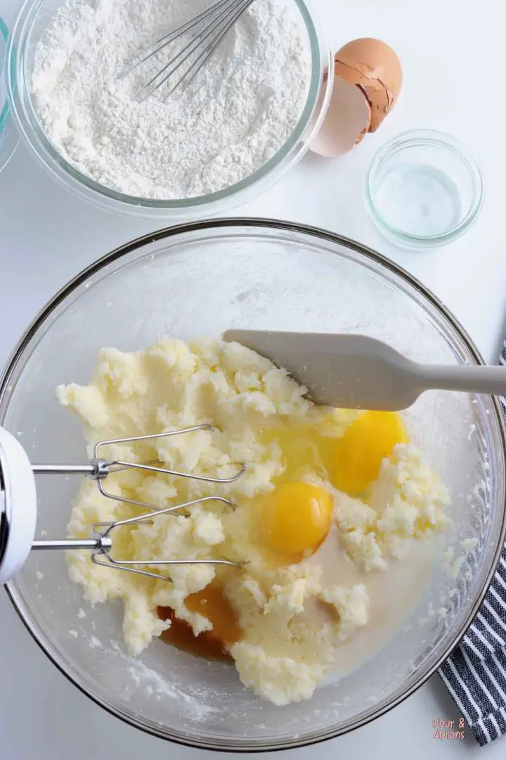 Bowl with creamed sugar and butter with eggs, milk and vanilla extract added to it.
