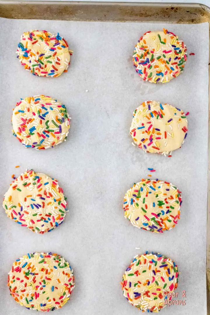 Cookie dough with sprinkles flattened on cookie sheet.