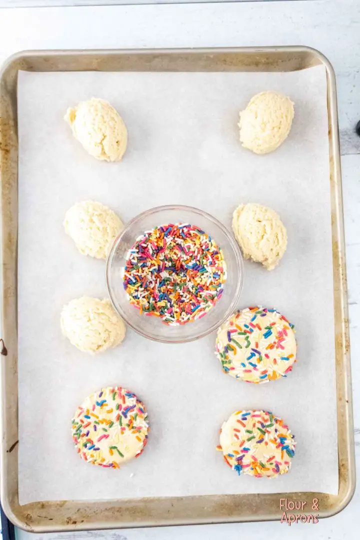 Balls of cookie dough on baking sheet with 3 of them flattened and with sprinkles added.