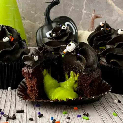 Cupcake with black frosting cut in half with green slime oozing out.
